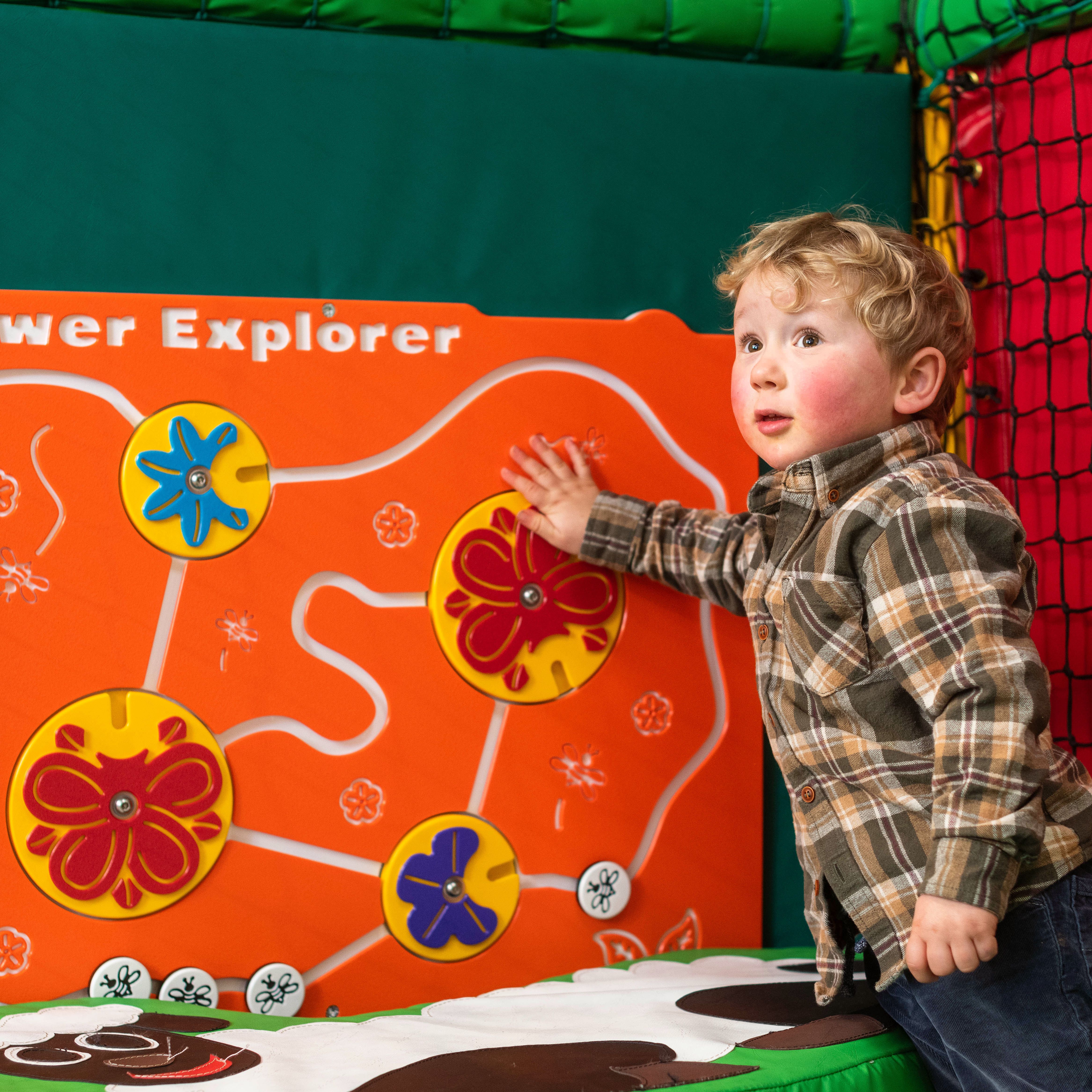 A young child playing with a colorful flower-themed activity board inside an indoor play area.