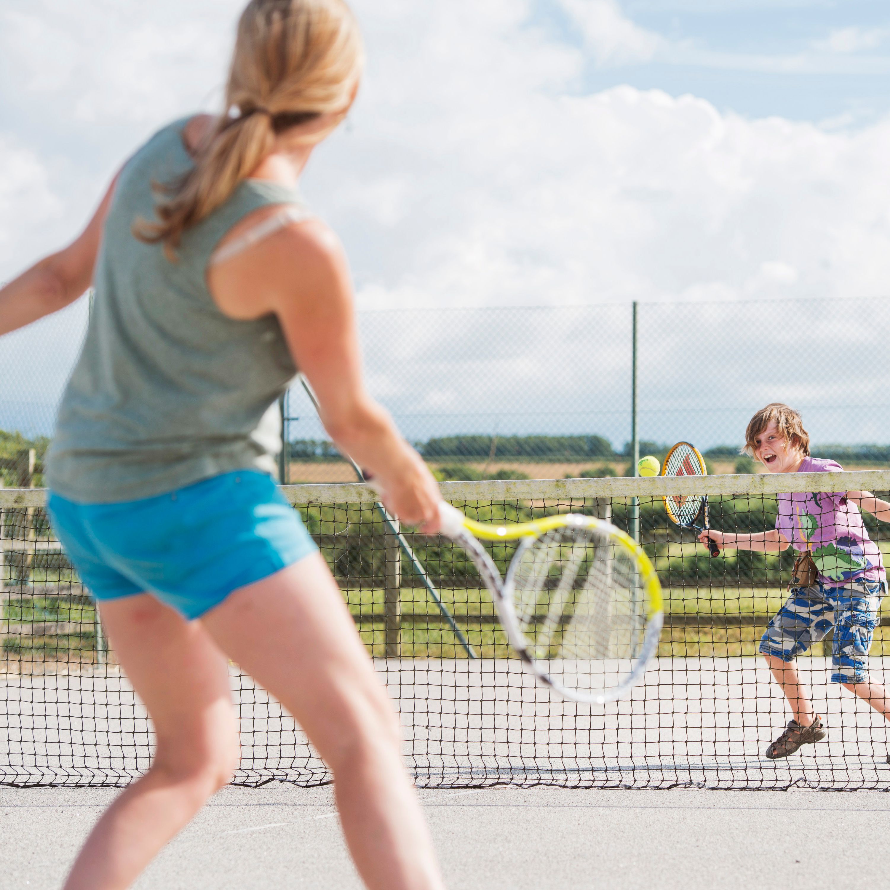 Woman and child playing tennis on an outdoor court on a sunny day.