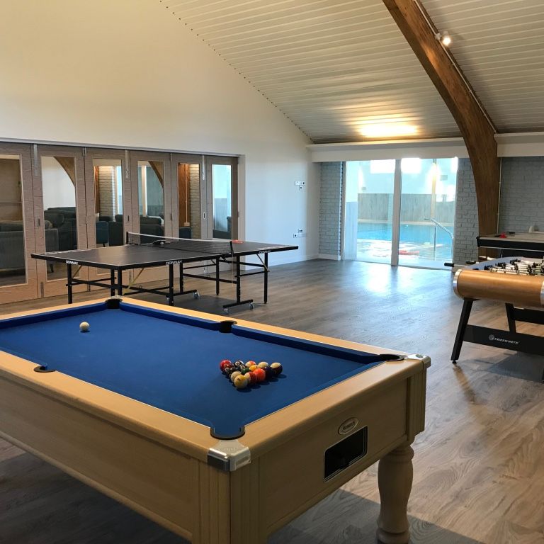 Spacious game room with a pool table, table tennis, foosball table, air hockey table, and glass doors leading to a swimming pool area.