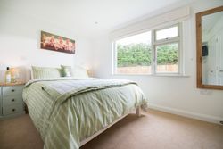 Bright bedroom with green striped bedding, a large window, a bedside table with a bottle of wine and glasses, a wall mirror, and a painting of piglets above the bed.