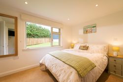Bright and cozy bedroom with large window, double bed with floral bedding, green throw blanket, two bedside tables with lamps, a painting above the bed, and a mirror on the wall.