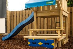 Wooden playground set with a blue slide, blue canopy, and a wooden fence in the background.
