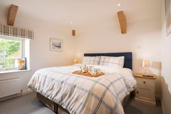 Cozy bedroom with a blue upholstered bed, plaid bedding, two bedside tables with lamps, a window with striped blinds, and a breakfast tray with cups and a teapot on the bed.