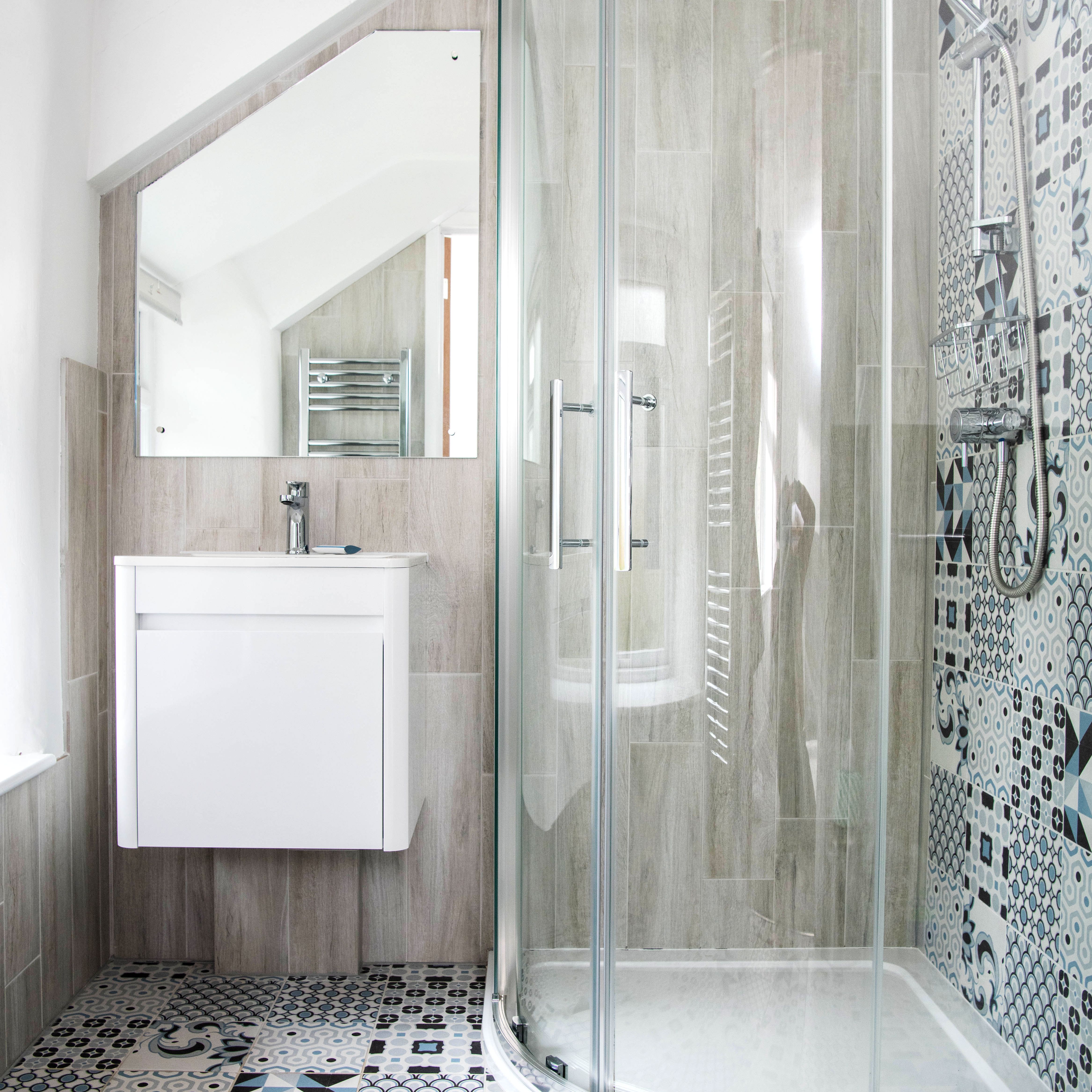 Modern bathroom with patterned tile floor, glass shower enclosure, wall-mounted sink, and large mirror.