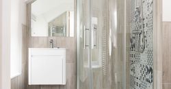 Modern bathroom with a glass shower enclosure, patterned tiles, a white vanity with a sink, and a large mirror.