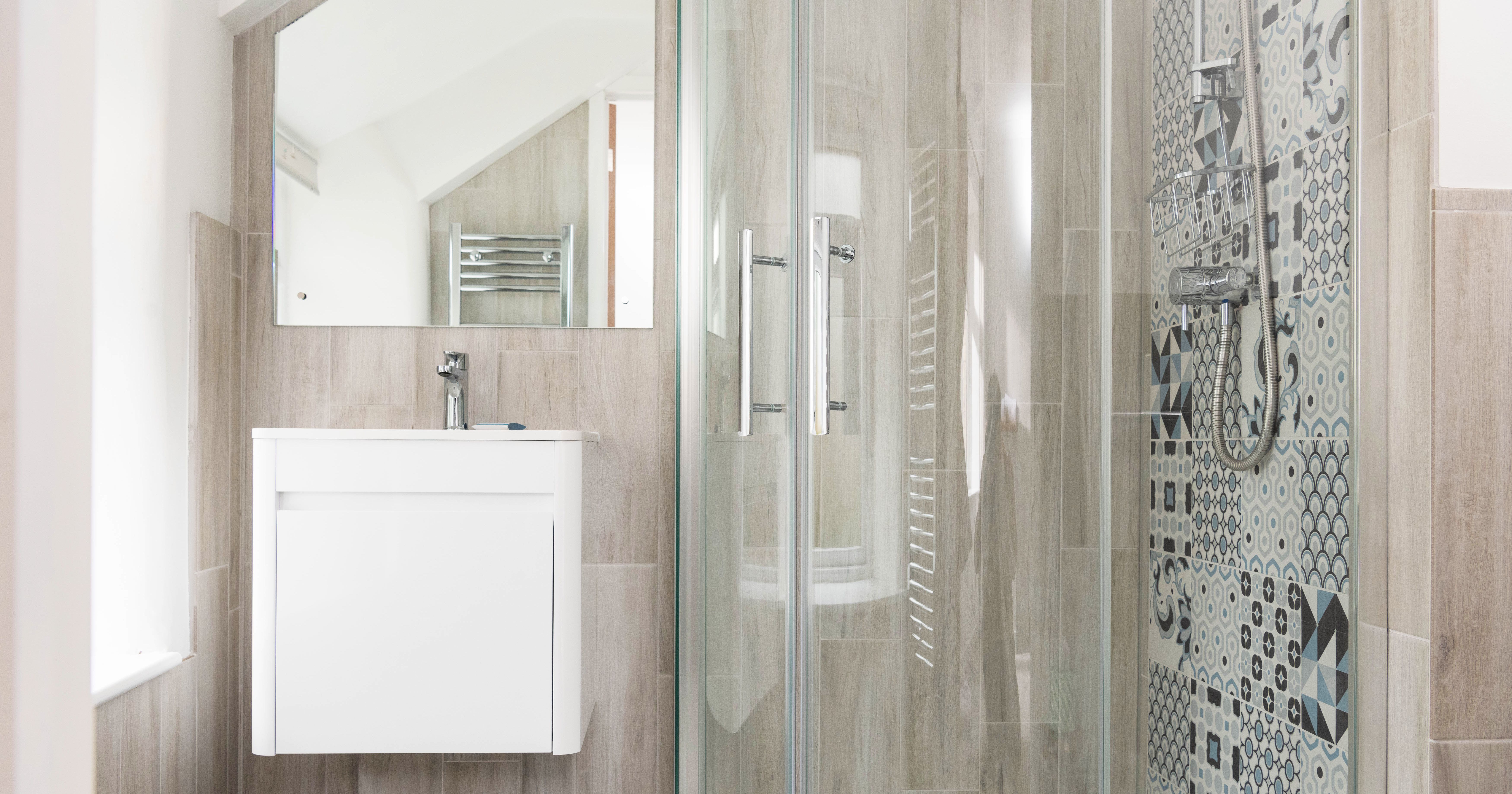 Modern bathroom with a glass shower enclosure, patterned tiles, a white vanity with a sink, and a large mirror.