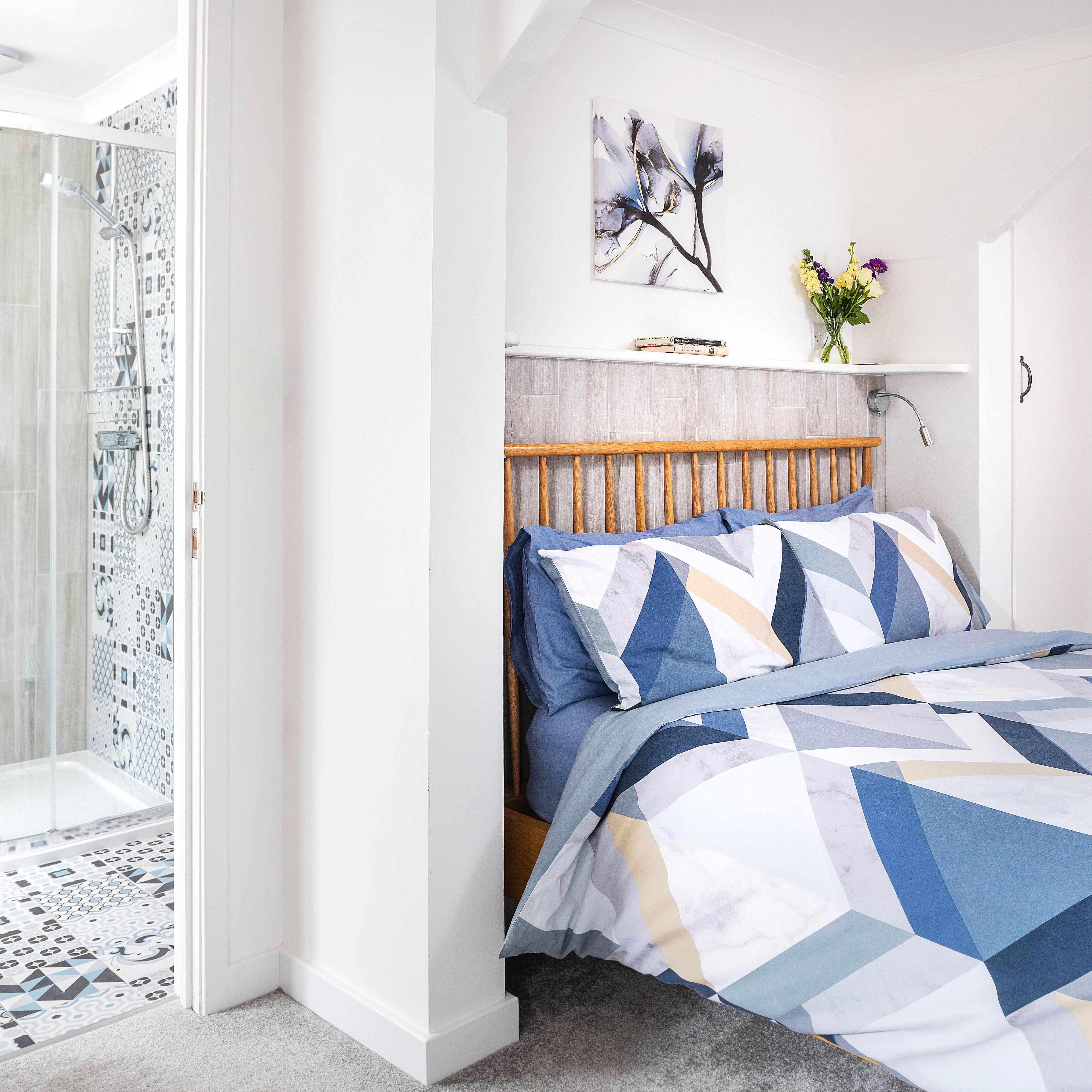 Modern bedroom with geometric blue and white bedding, wooden headboard, and en-suite bathroom with patterned tiles and glass shower enclosure.