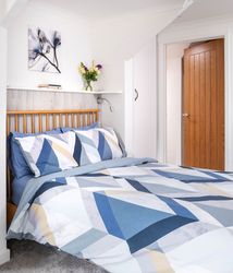 Modern bedroom with geometric blue and white bedding, wooden headboard, and en-suite bathroom with patterned tiles and glass shower enclosure.