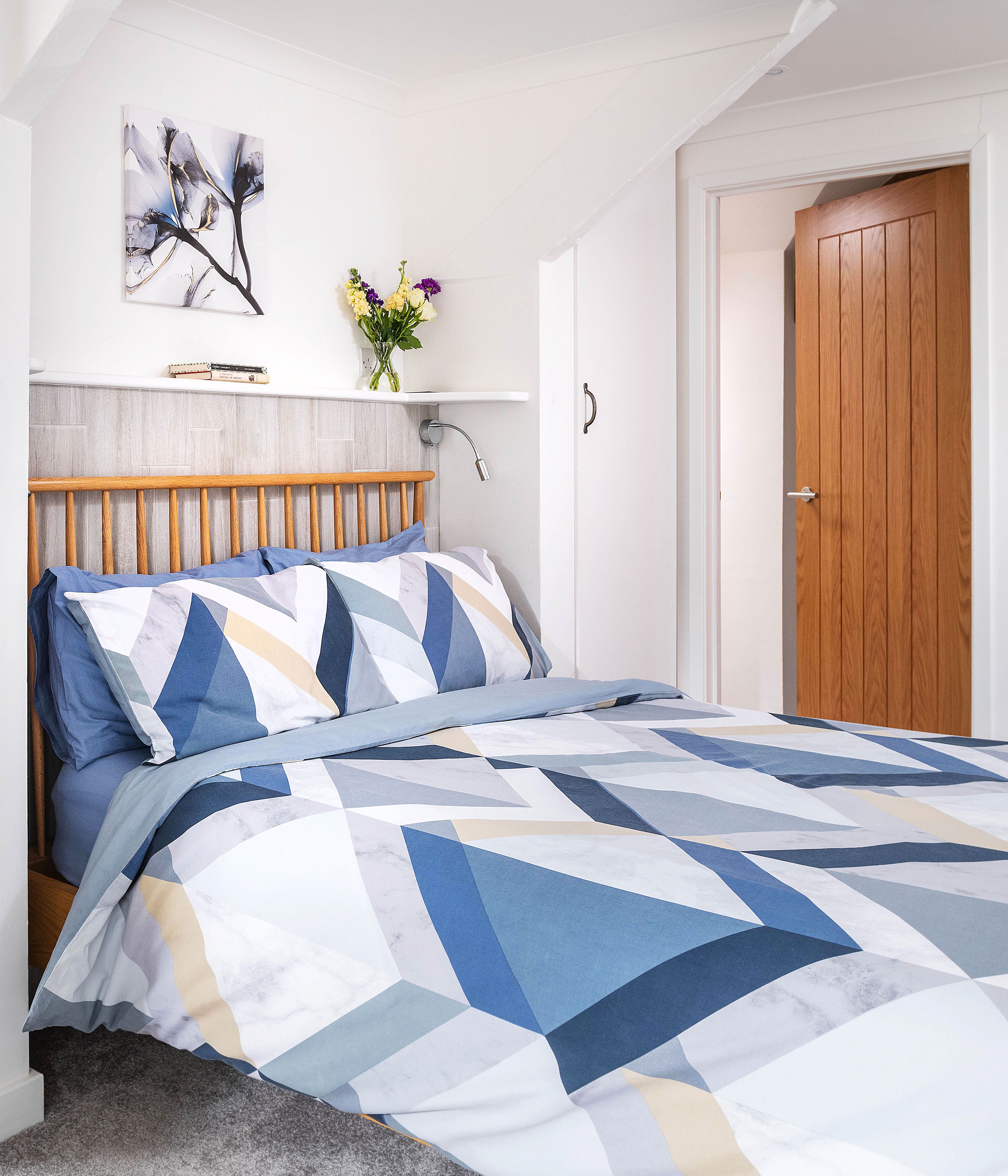 Modern bedroom with geometric blue and white bedding, wooden headboard, and en-suite bathroom with patterned tiles and glass shower enclosure.