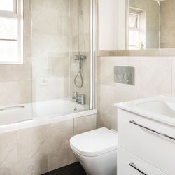 Modern bathroom with a bathtub, shower, wall-mounted toilet, white vanity with sink, large mirror, and a small vase with purple flowers on the window sill.