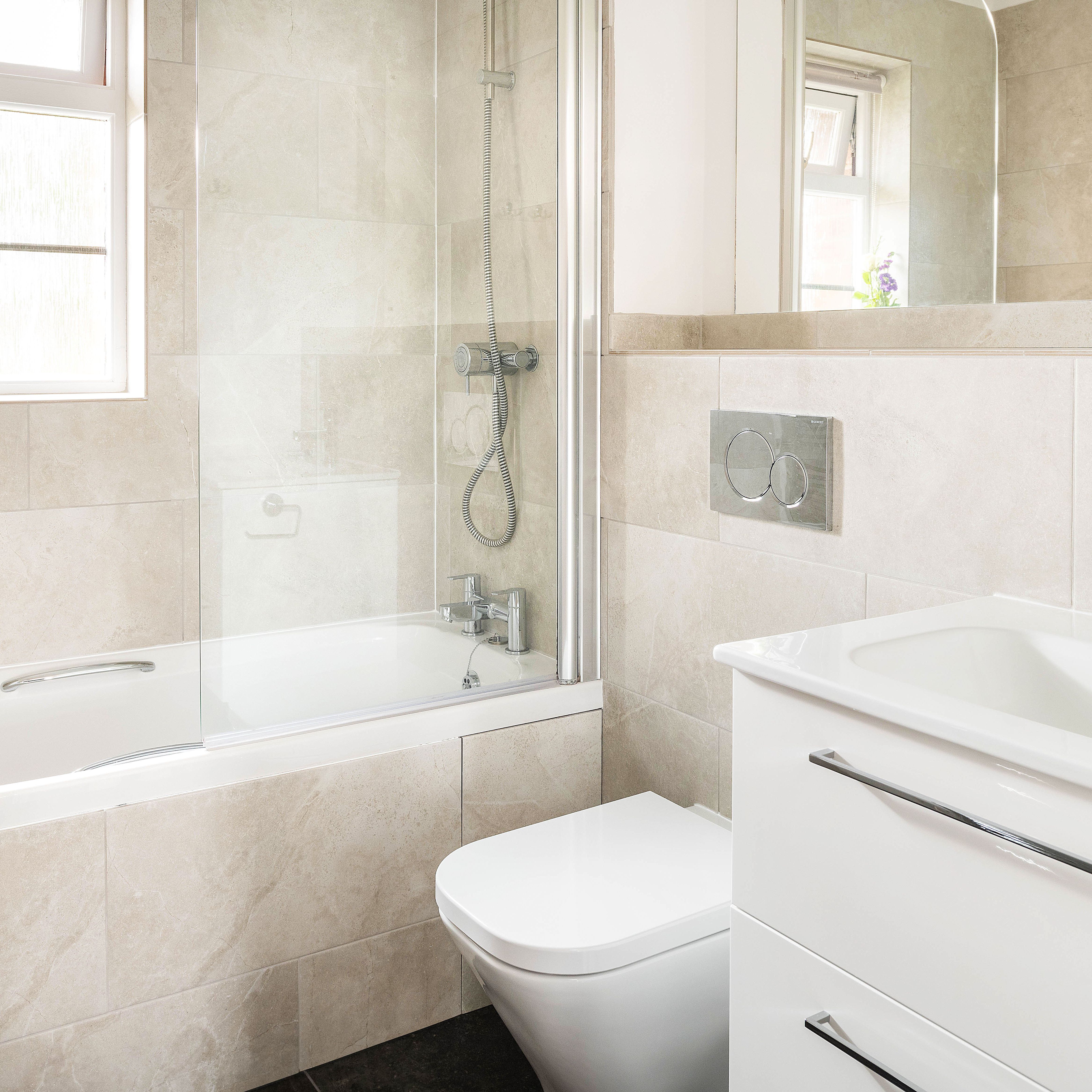 Modern bathroom with a bathtub, shower, wall-mounted toilet, white vanity with sink, large mirror, and a small vase with purple flowers on the window sill.