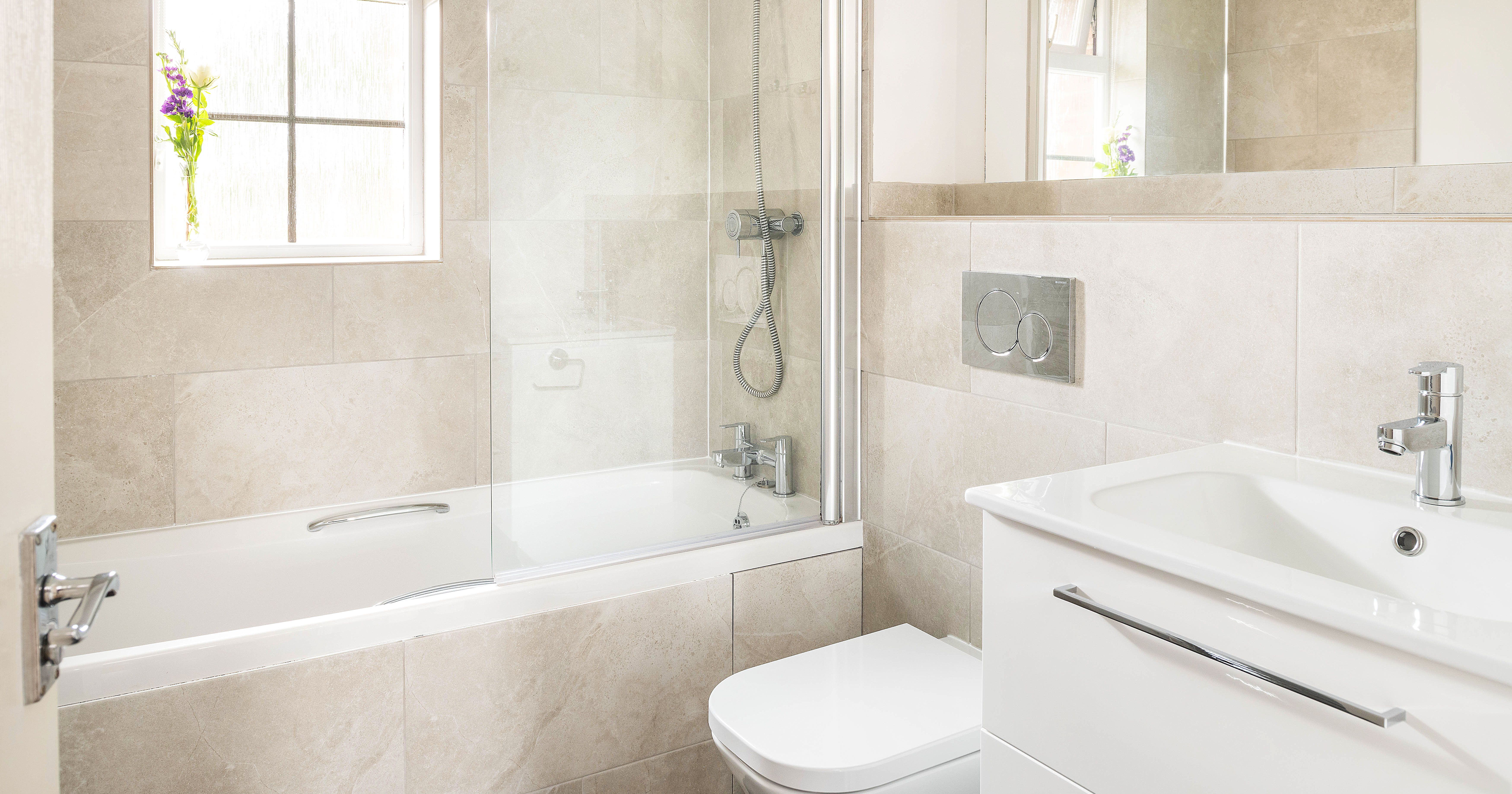 Modern bathroom with a bathtub, shower, wall-mounted toilet, white vanity with sink, large mirror, and a small vase with purple flowers on the window sill.