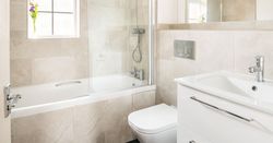 Modern bathroom with a bathtub, shower, wall-mounted toilet, white vanity with sink, large mirror, and a small vase with purple flowers on the window sill.