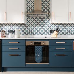 Modern kitchen with blue cabinets, patterned tile backsplash, white upper cabinets, stainless steel oven, and kitchen appliances on the countertop.