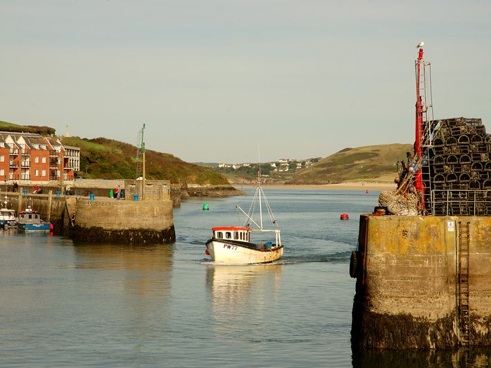 Fishing boat entering Padstow harbour between stone piers with lobster pots stacked on the right.