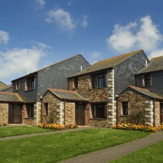 Row of modern stone houses with slate roofs, front lawns, and flower beds under a blue sky.