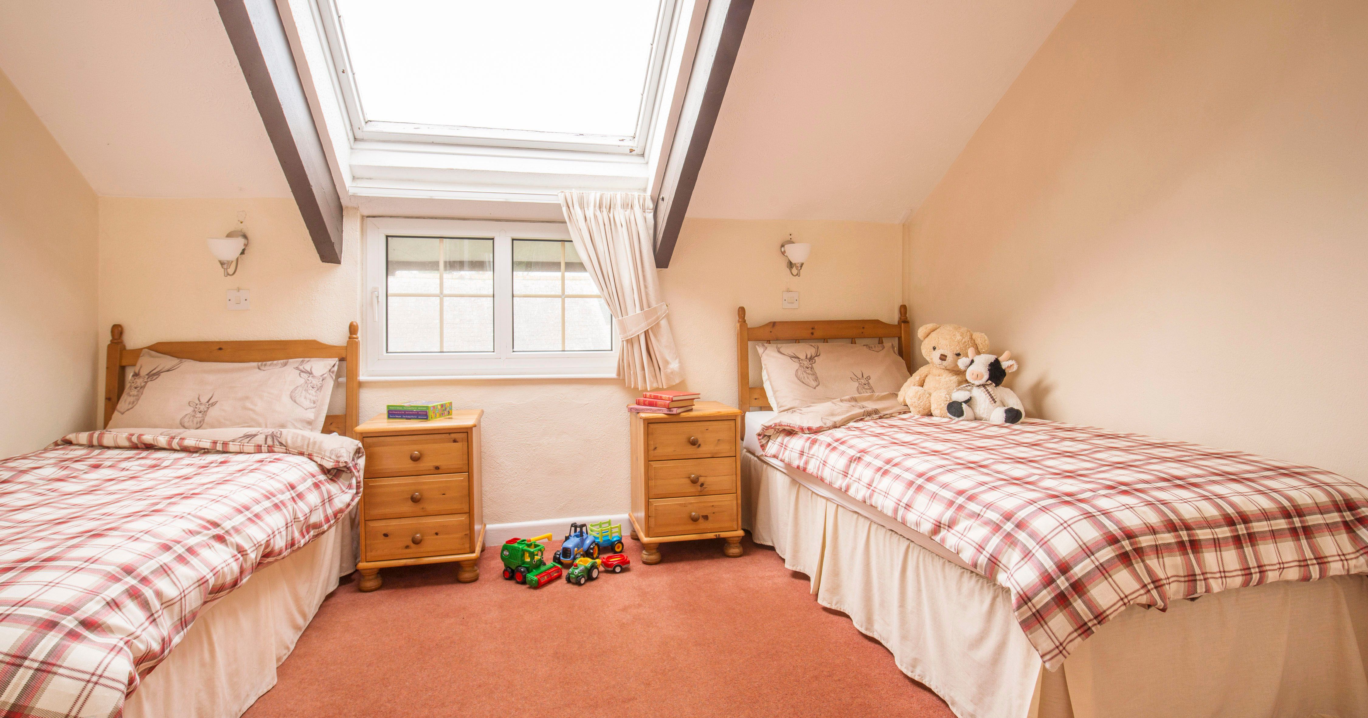 Cozy attic bedroom with two single beds, plaid bedding, skylight, toys on the floor, and stuffed animals on one bed.