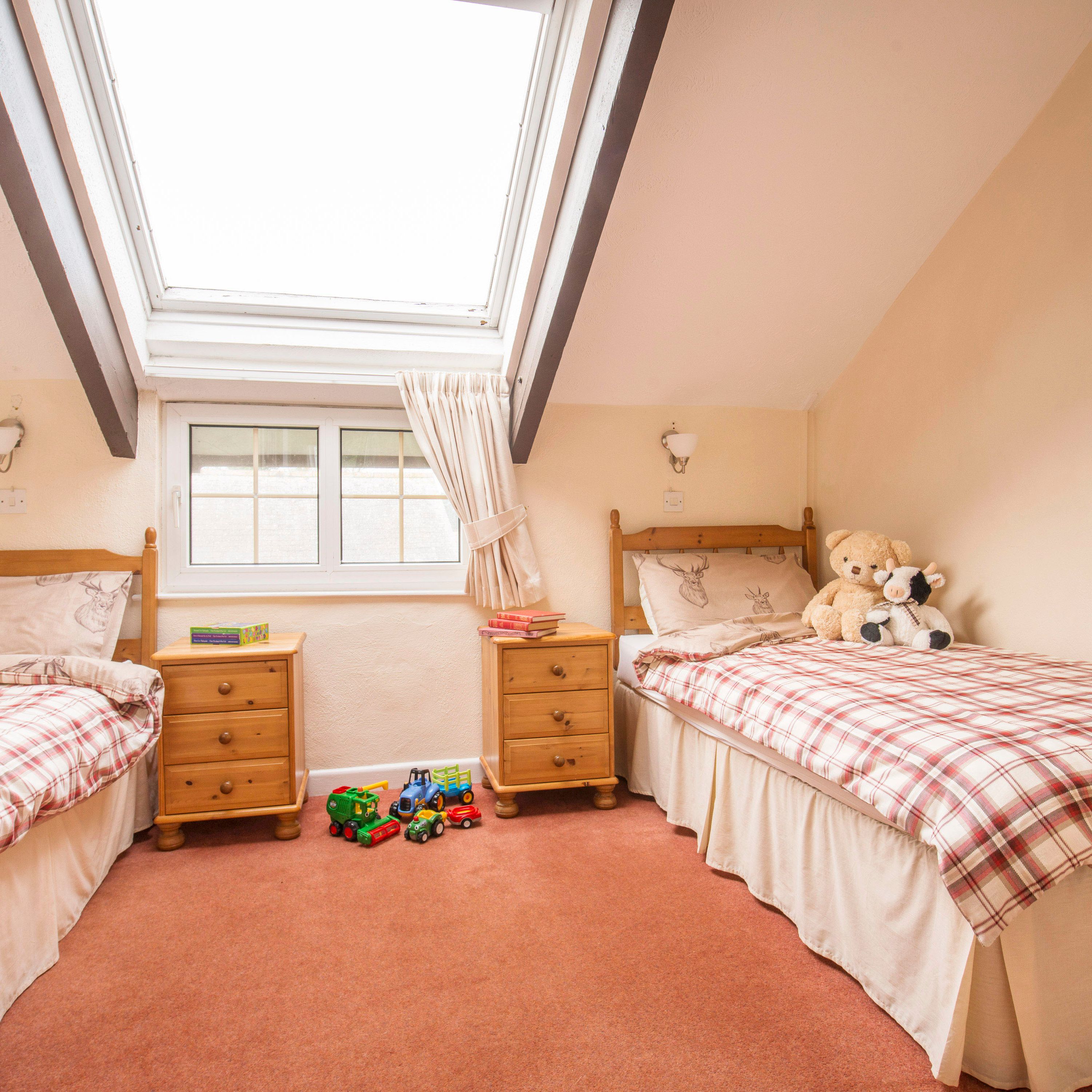 Cozy attic bedroom with two single beds, plaid bedding, skylight, toys on the floor, and stuffed animals on one bed.