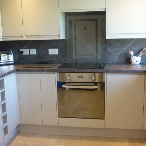 Modern kitchen with grey countertops, built-in oven, electric stove, toaster, and decorative utensils on the counter.