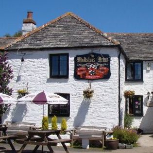 White stone building with the sign 'Maltsters Arms', outdoor seating, and umbrellas.
