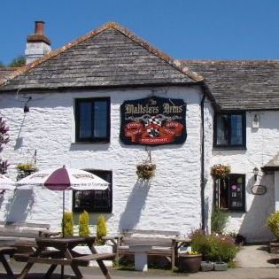 White stone building with the sign 'Maltsters Arms', outdoor seating, and umbrellas.