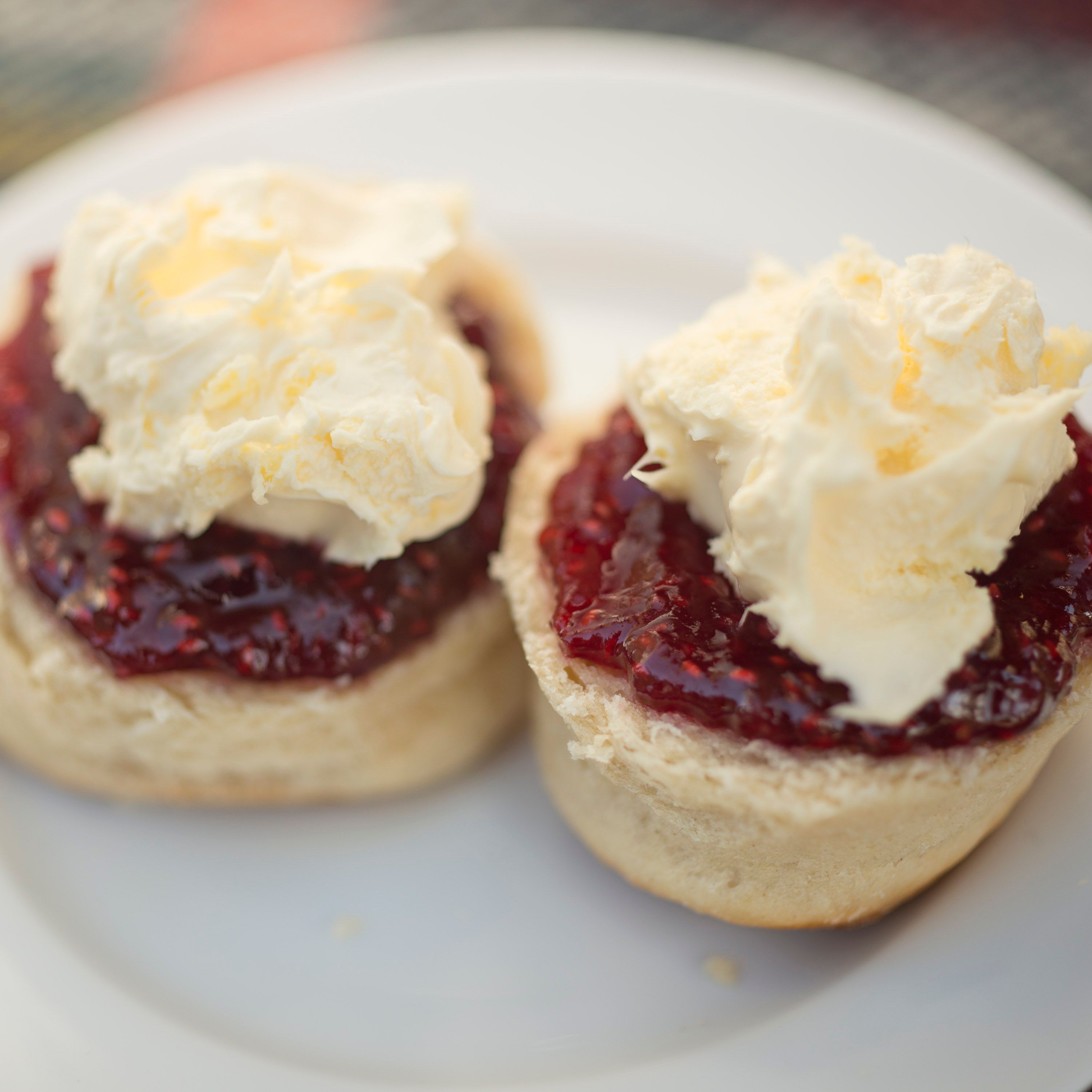 Two scones topped with strawberry jam and clotted cream on a white plate.