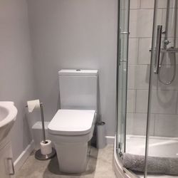 Modern bathroom with a toilet, a sink, a glass-enclosed shower, and a floor mat.