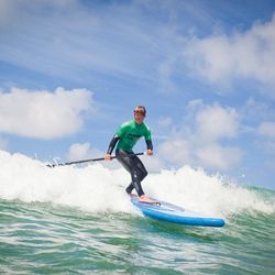 Person paddleboarding on a wave in the ocean under a partly cloudy sky.