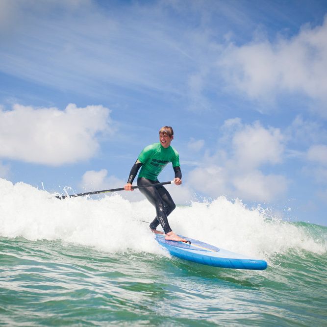 Person paddleboarding on a wave in the ocean under a partly cloudy sky.
