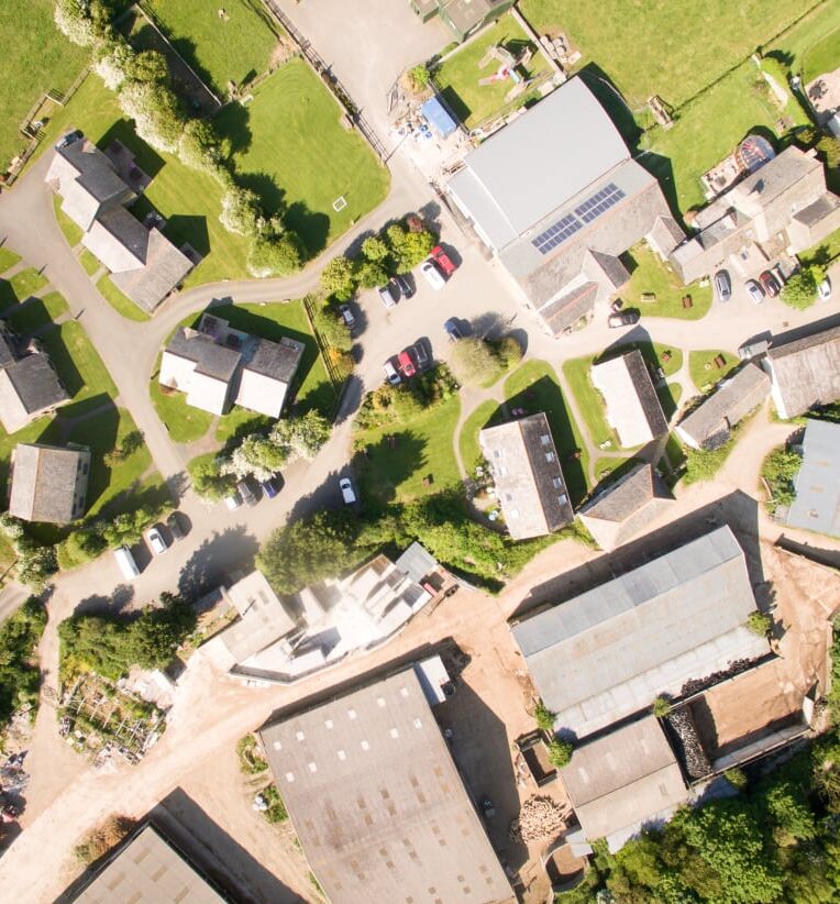 Aerial view of a rural village with houses, roads, green lawns, trees, and surrounding farmland.