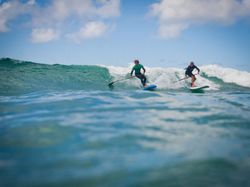 Two people stand-up paddleboarding on ocean waves under a blue sky with some clouds.