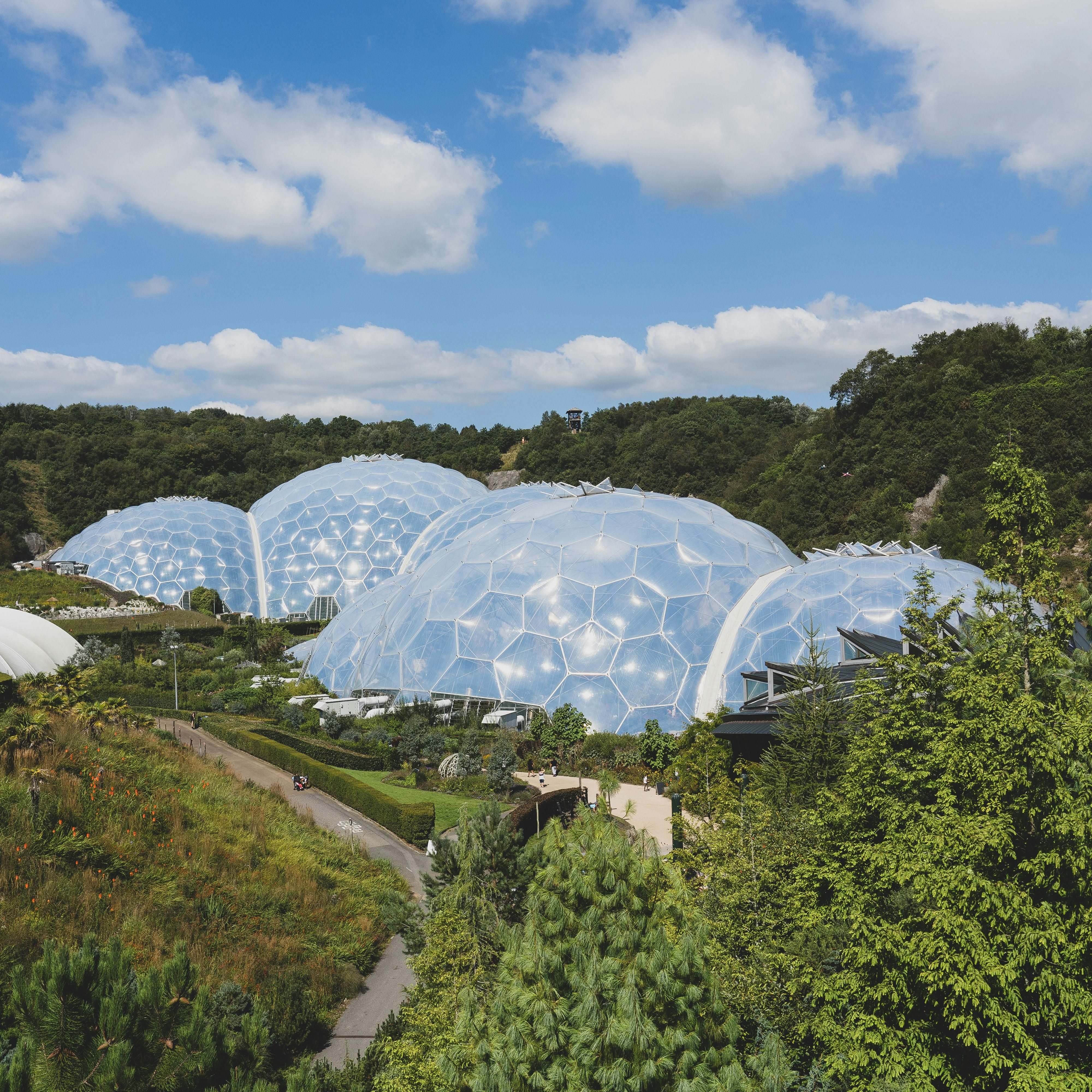 View of large geodesic biodomes surrounded by lush green vegetation under a blue sky with scattered clouds.