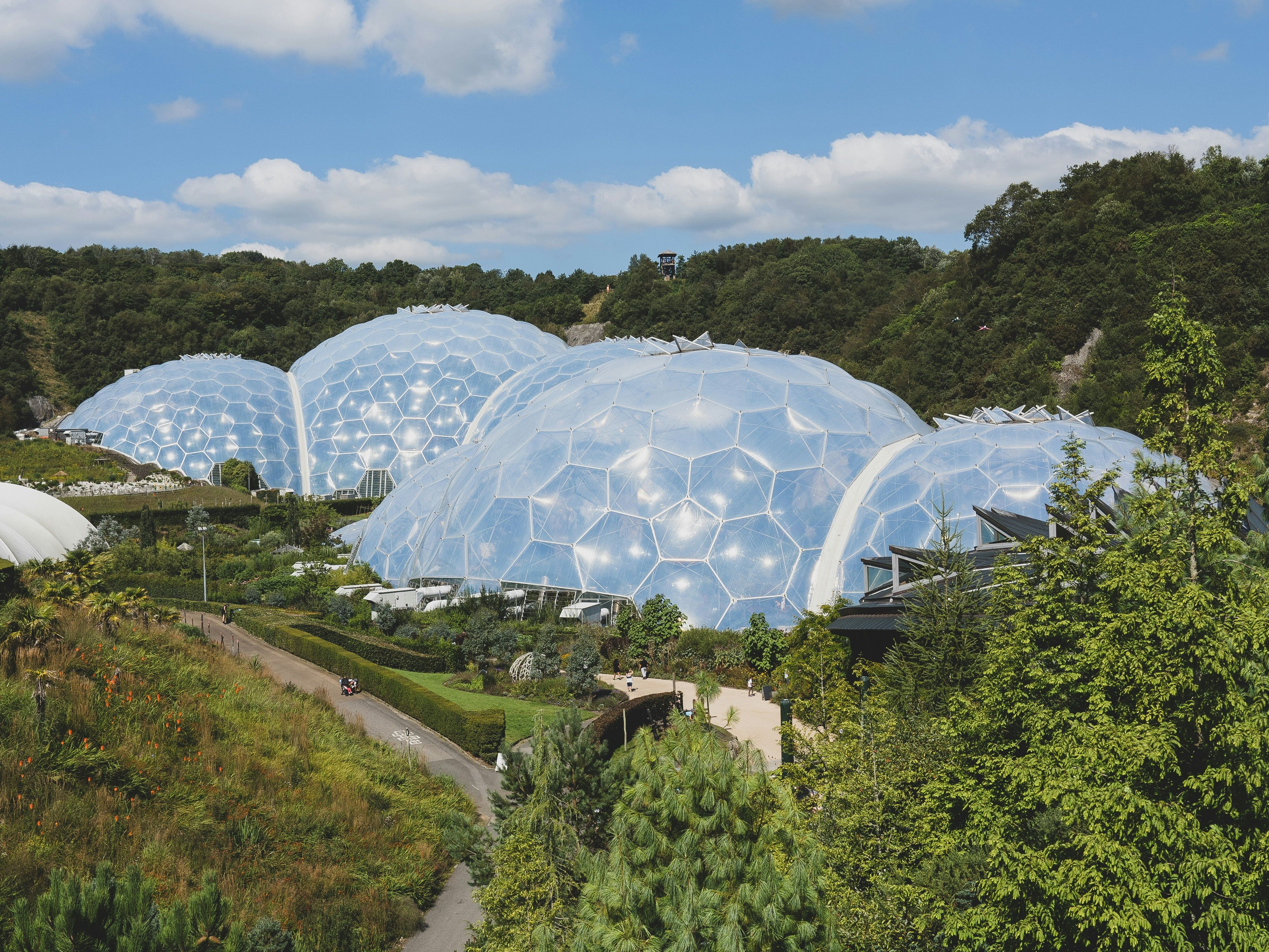 View of large geodesic biodomes surrounded by lush green vegetation under a blue sky with scattered clouds.