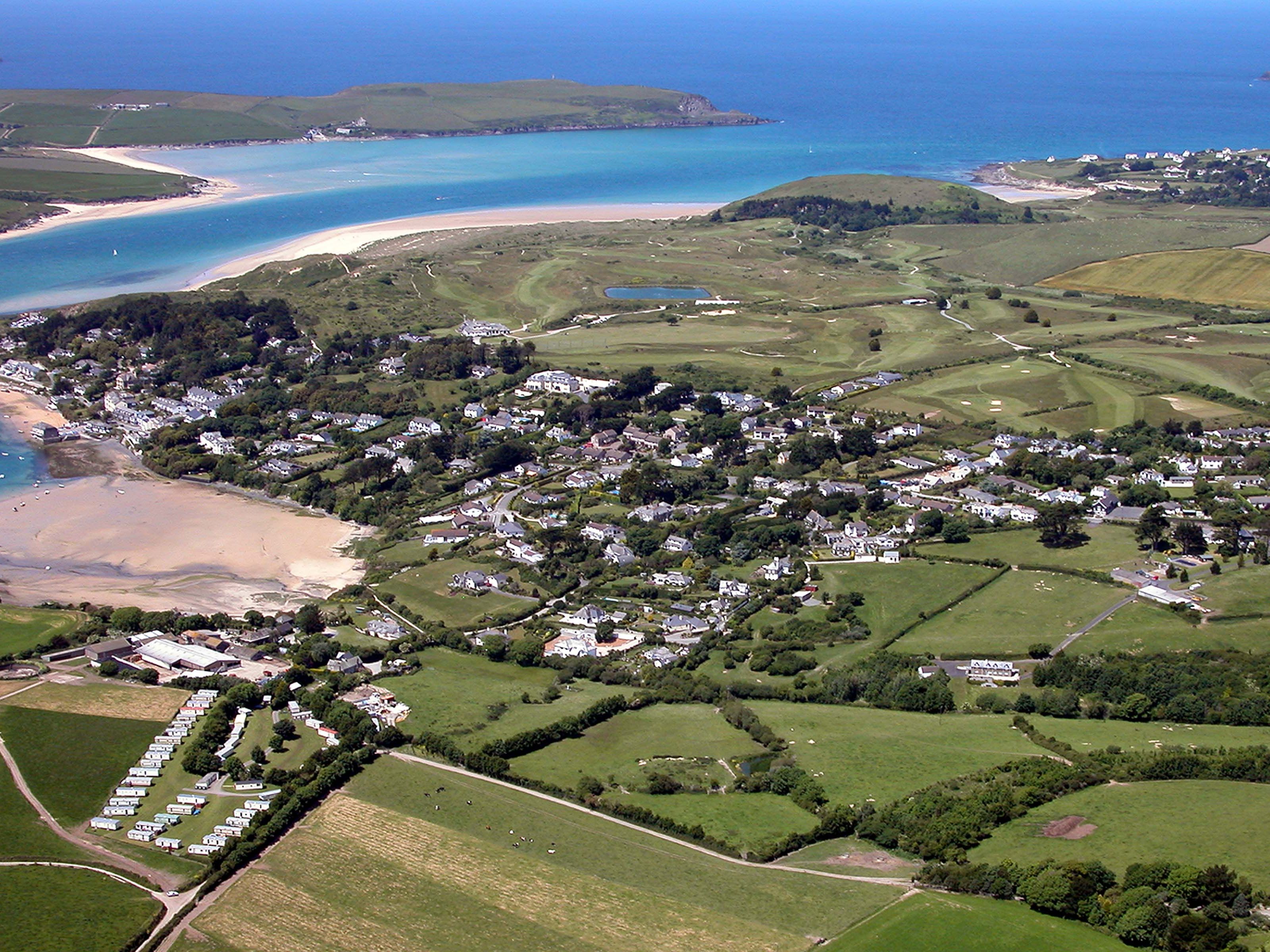 Aerial view of a coastal village with sandy beach, green fields, scattered houses, and a river flowing into the sea.