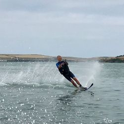 Person water skiing on a lake, creating a spray of water behind them with hills in the background.
