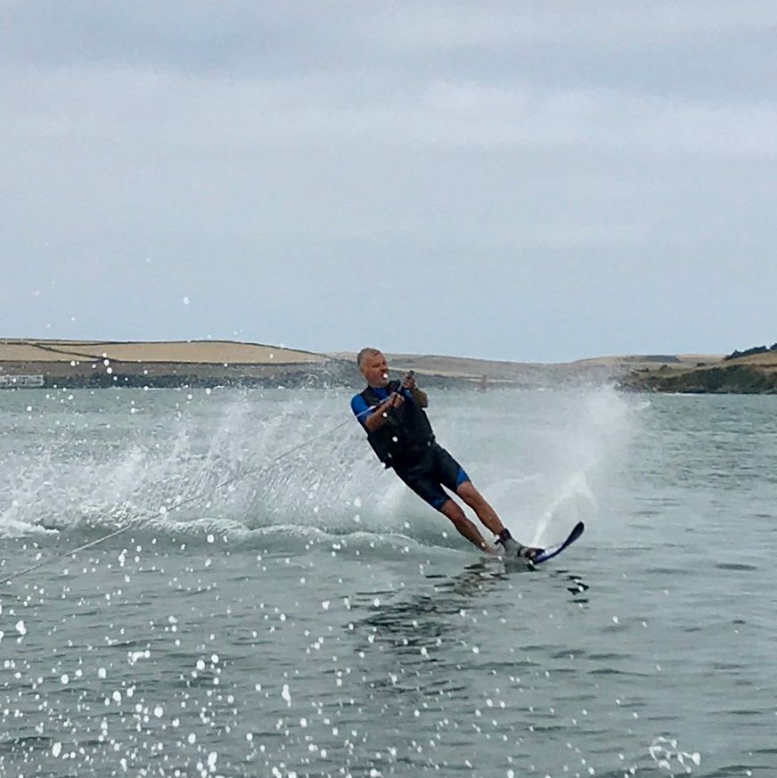 Person water skiing on a lake, creating a spray of water behind them with hills in the background.