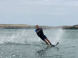 Person water skiing on a lake, creating a spray of water behind them with hills in the background.
