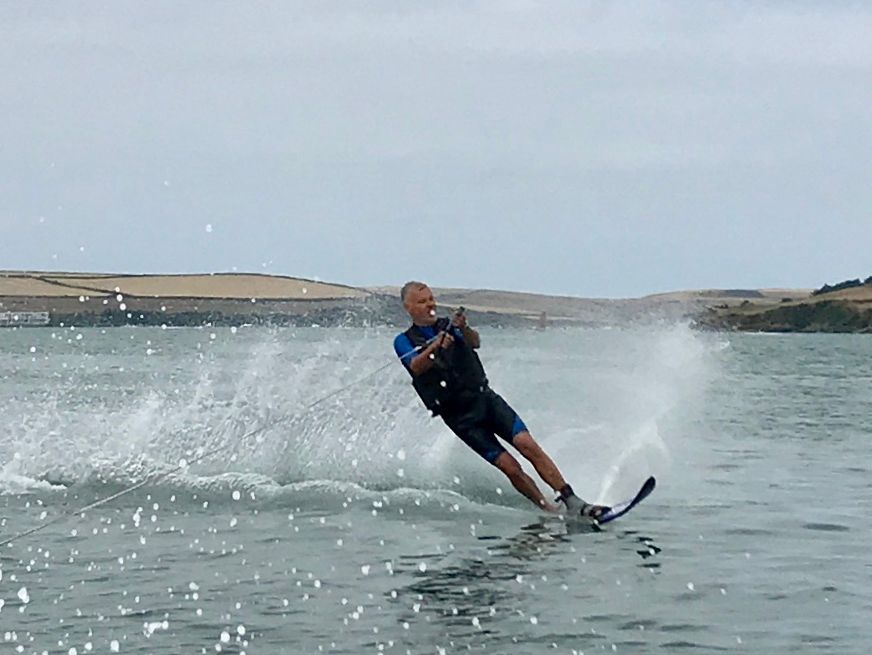Person water skiing on a lake, creating a spray of water behind them with hills in the background.