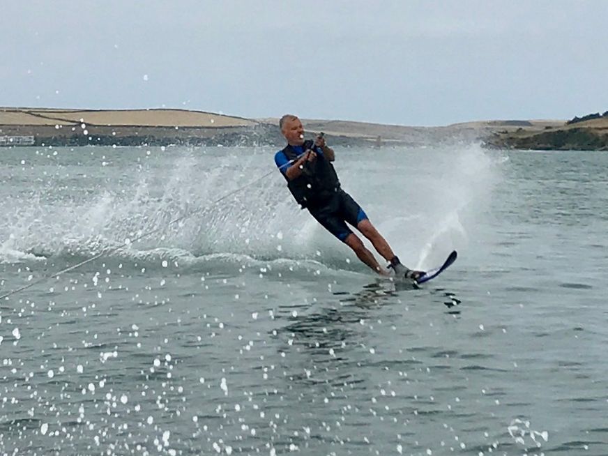 Person water skiing on a lake, creating a spray of water behind them with hills in the background.