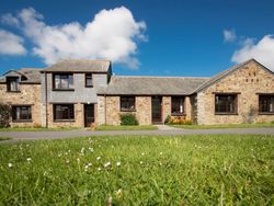 Stone farmhouse with dormer windows and grassy lawn under a blue sky