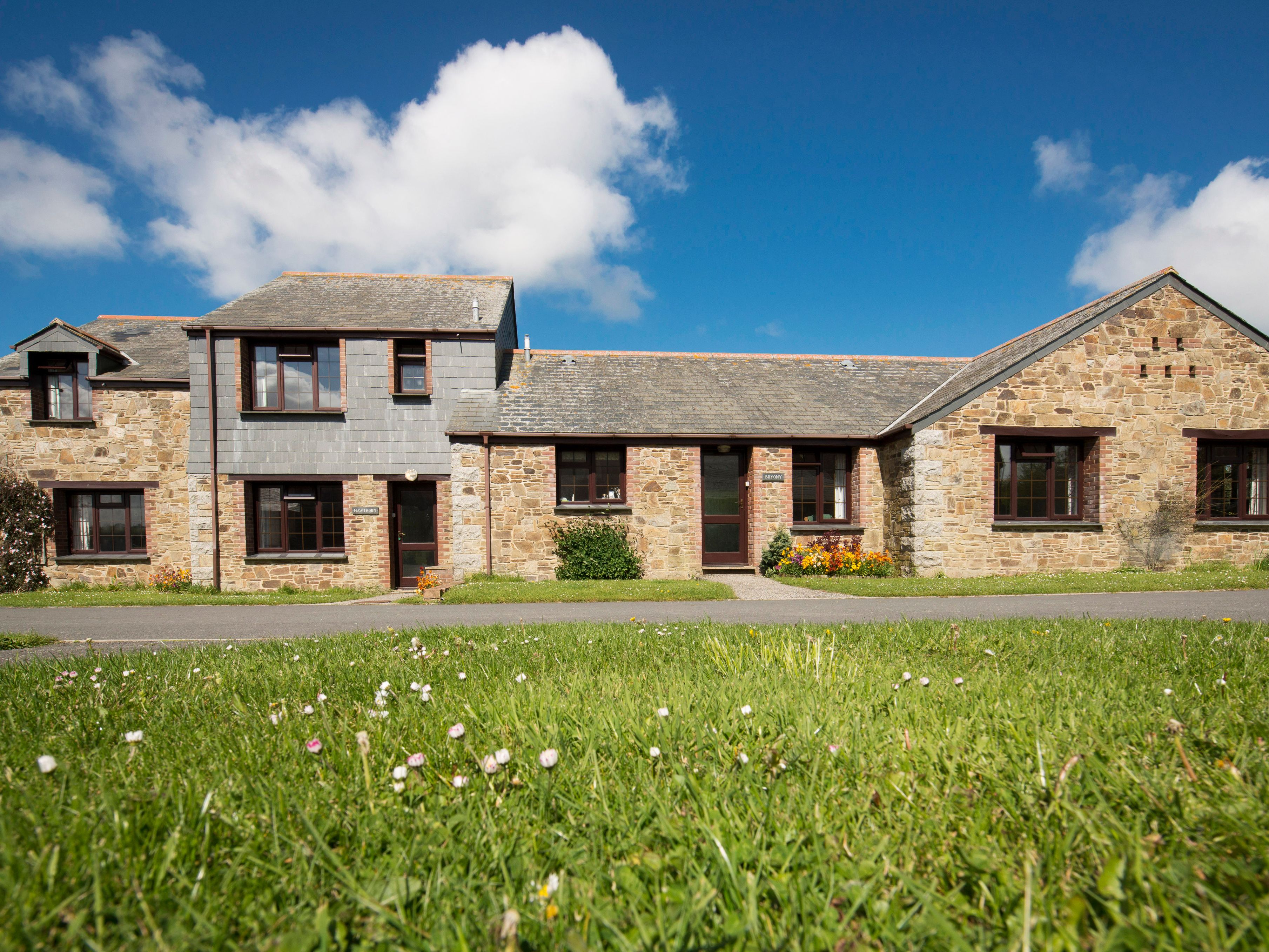 Stone farmhouse with dormer windows and grassy lawn under a blue sky