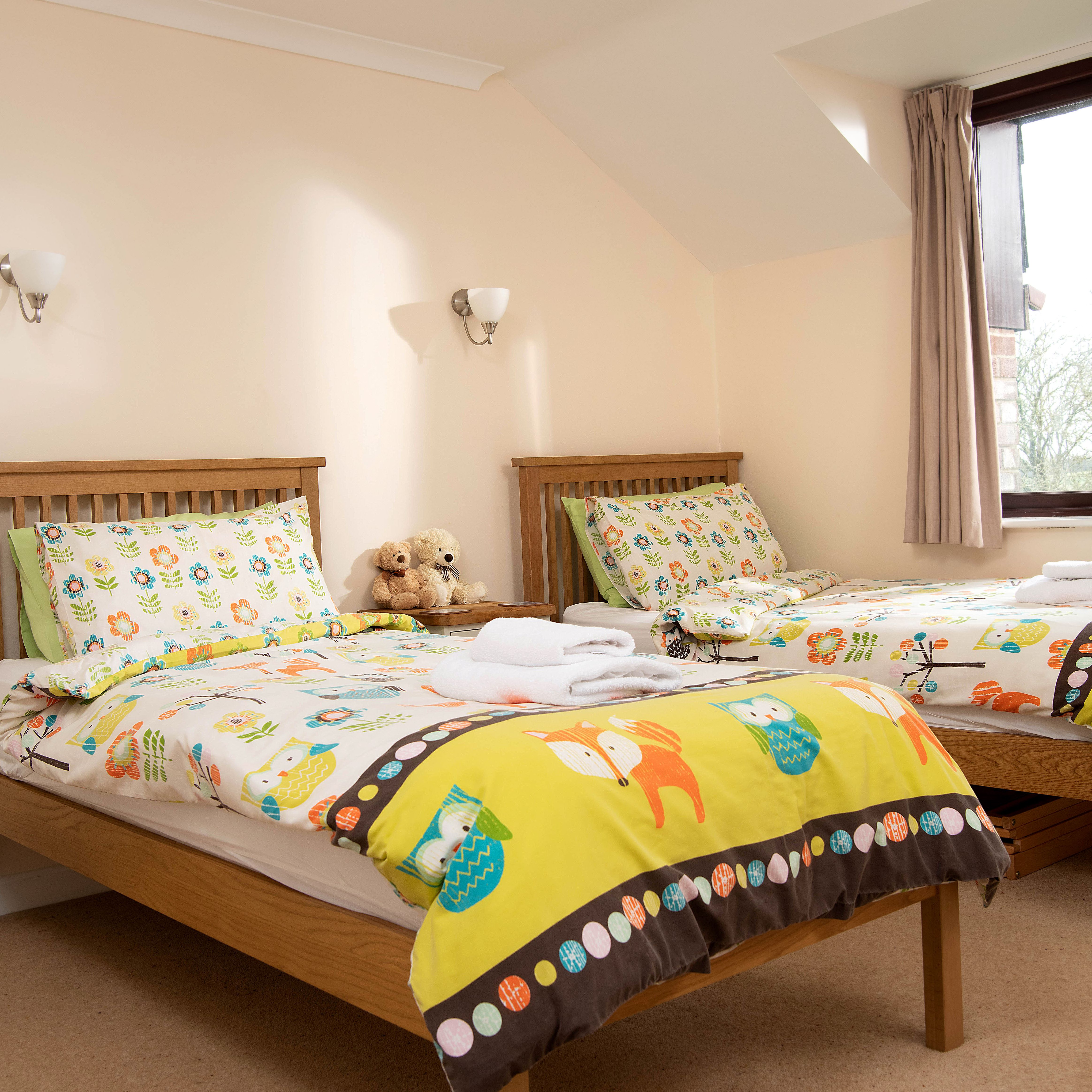 Bedroom with two single beds featuring colorful animal-themed bedding and a window letting in natural light.