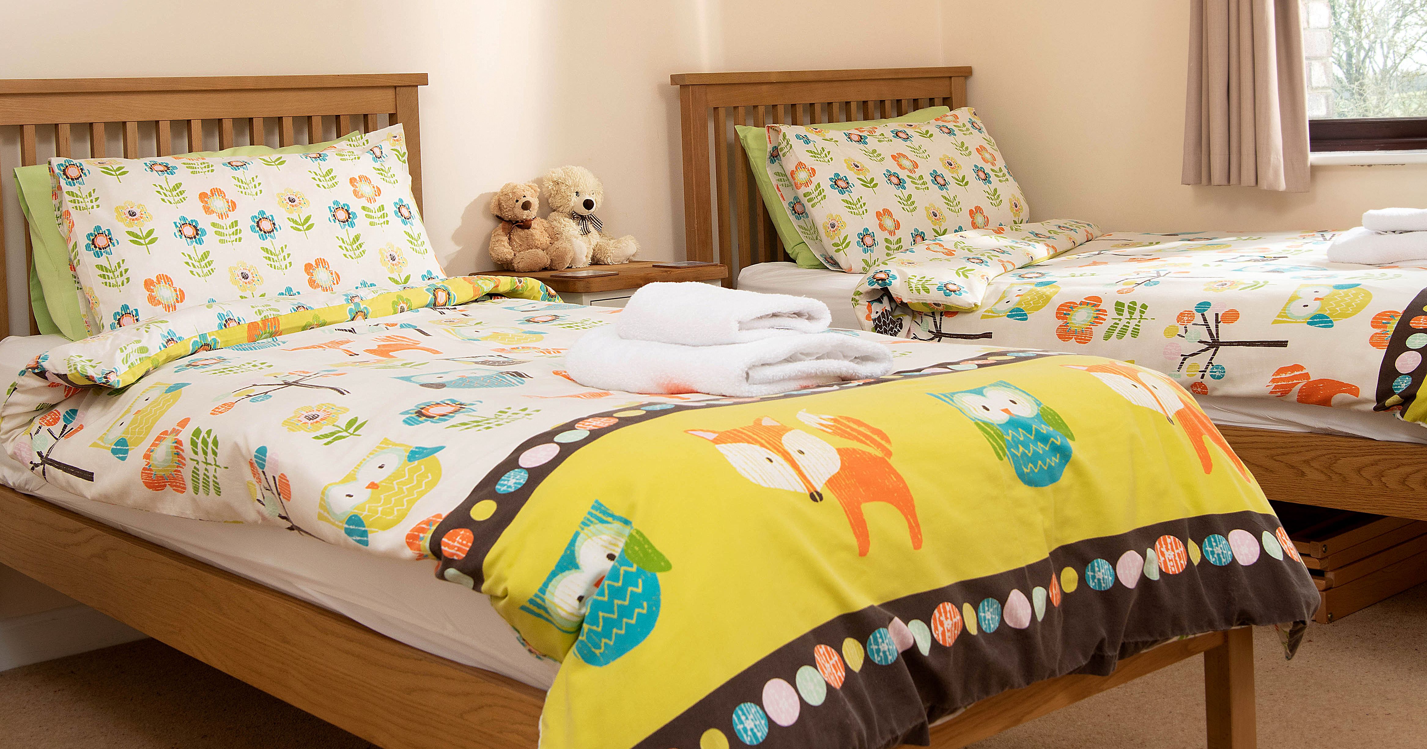 Bedroom with two single beds featuring colorful animal-themed bedding and a window letting in natural light.