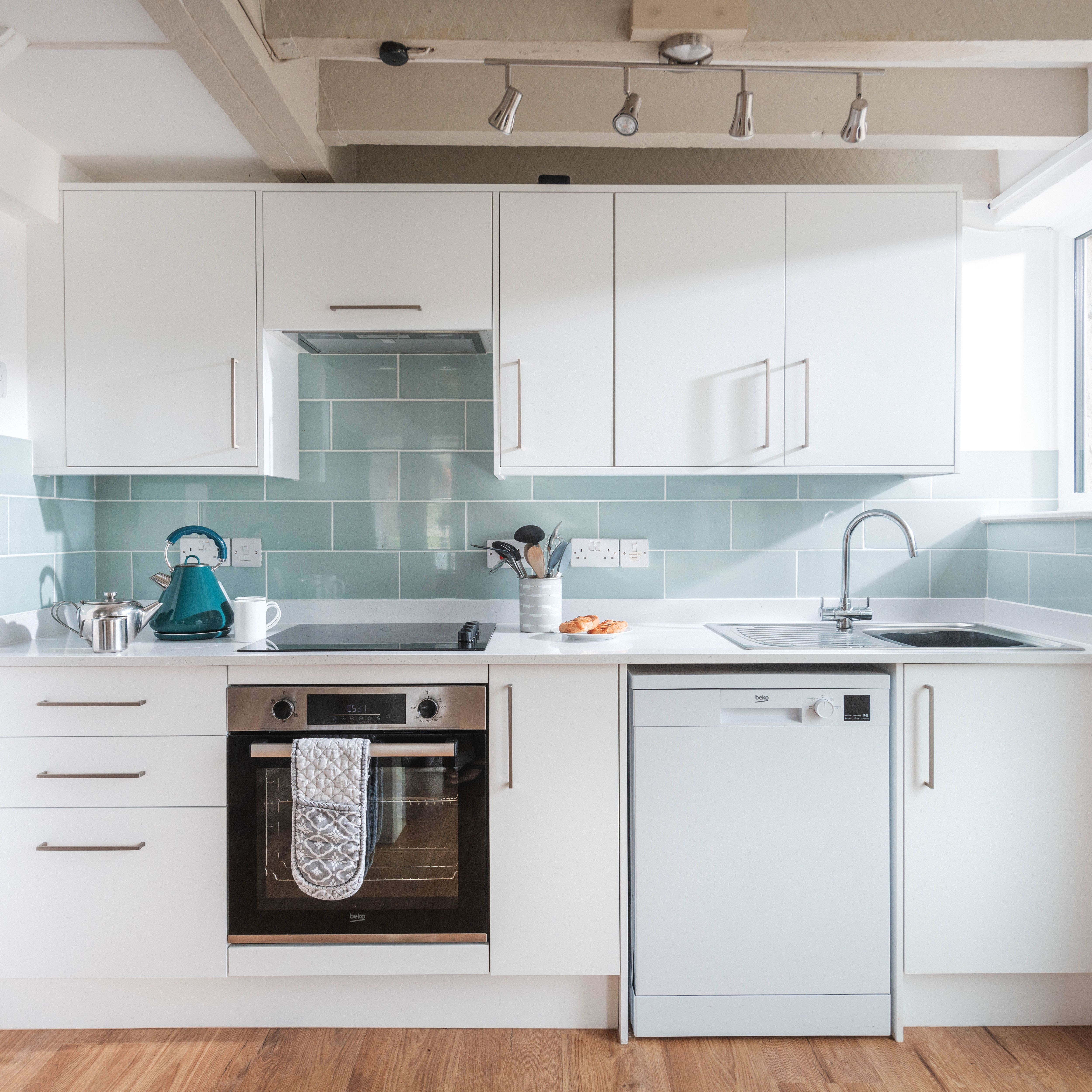 Modern white kitchen with light blue backsplash, stainless steel appliances, and wooden floor