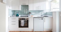 Modern white kitchen with light blue backsplash, stainless steel appliances, and wooden floor