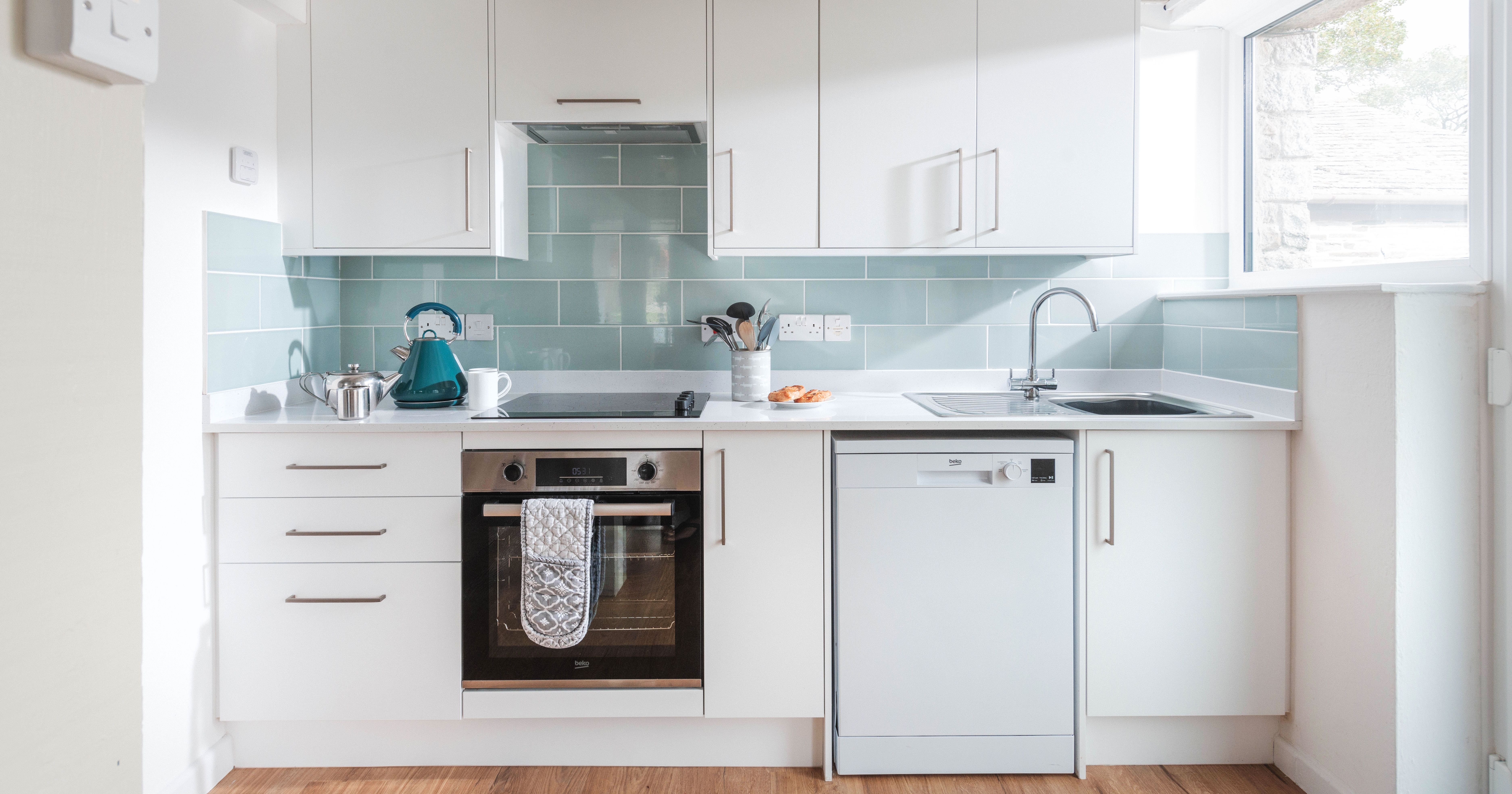 Modern white kitchen with light blue backsplash, stainless steel appliances, and wooden floor