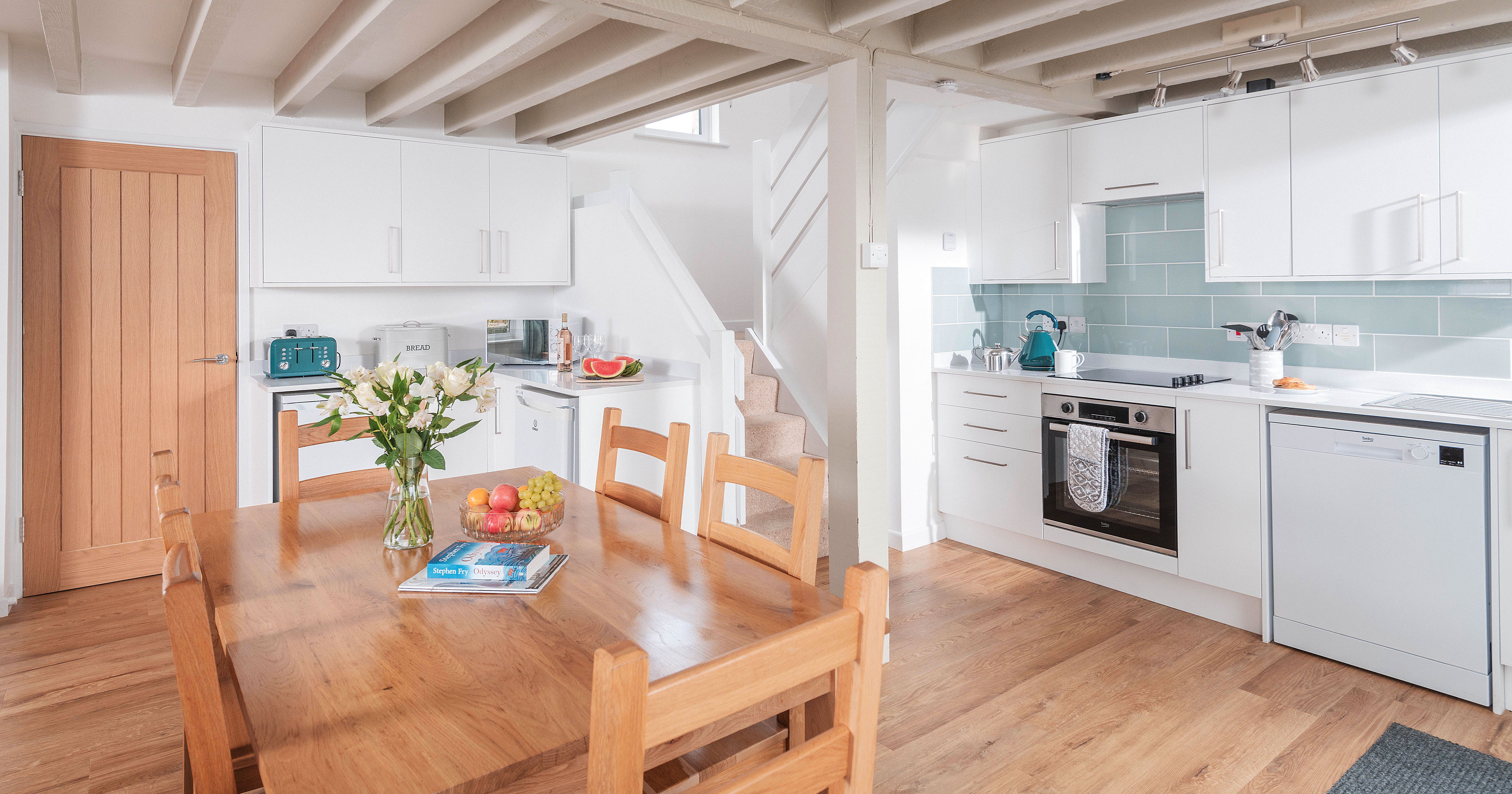 Modern kitchen and dining area with wooden table, white cabinets, and exposed ceiling beams