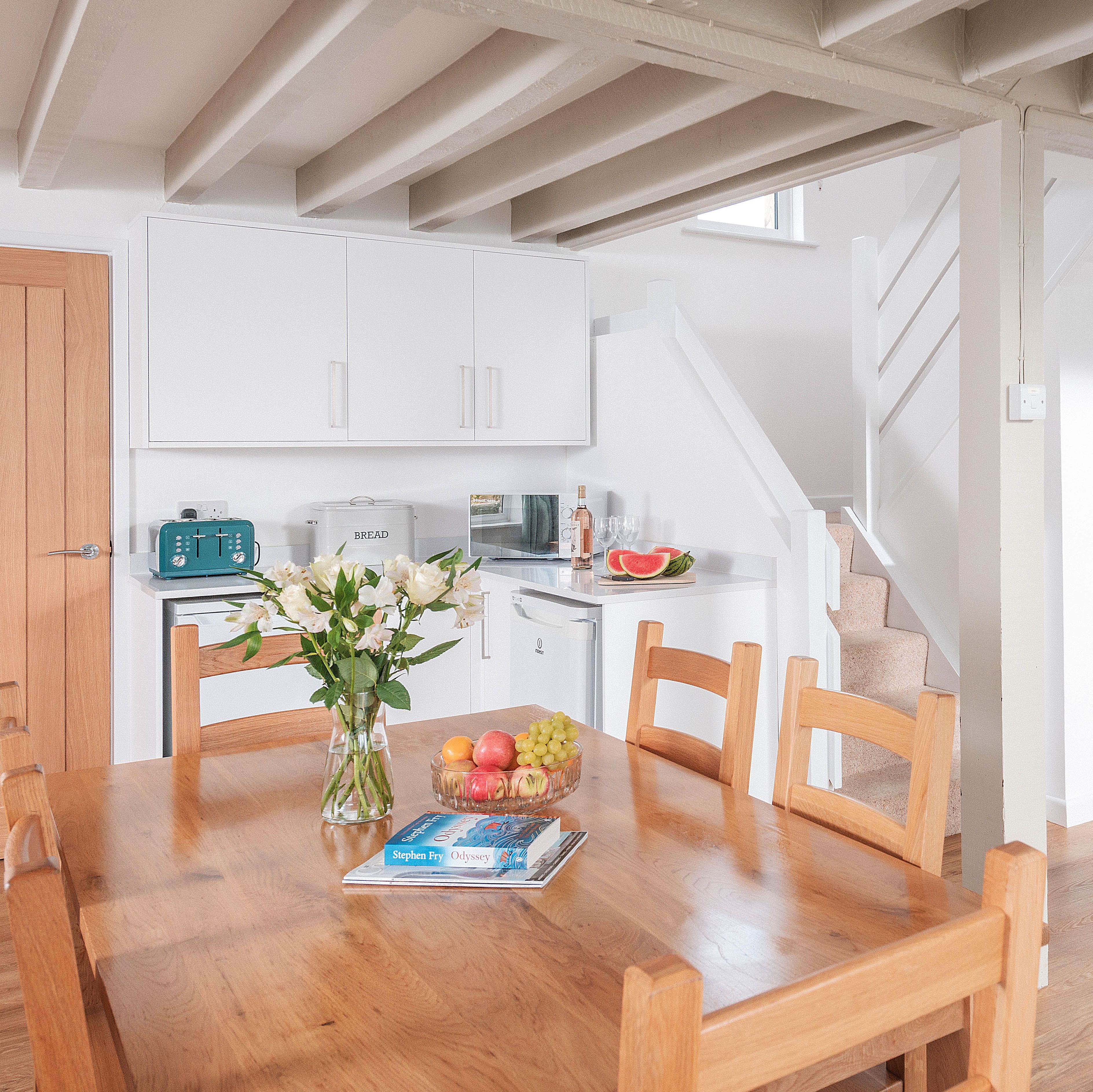 Modern kitchen and dining area with wooden table, white cabinets, and exposed ceiling beams