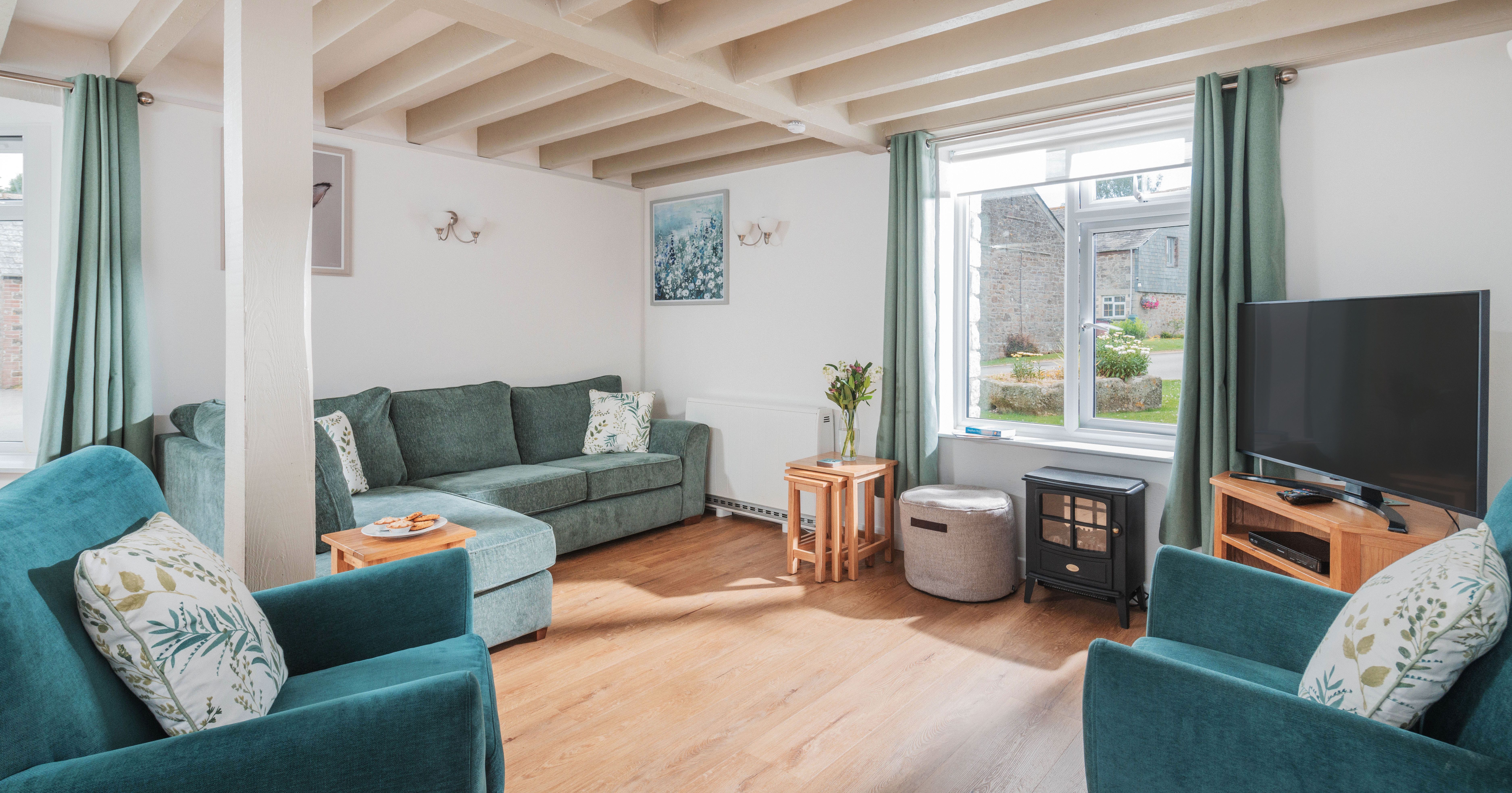 Cozy living room with green sofas, wooden floor, TV, and large window with green curtains
