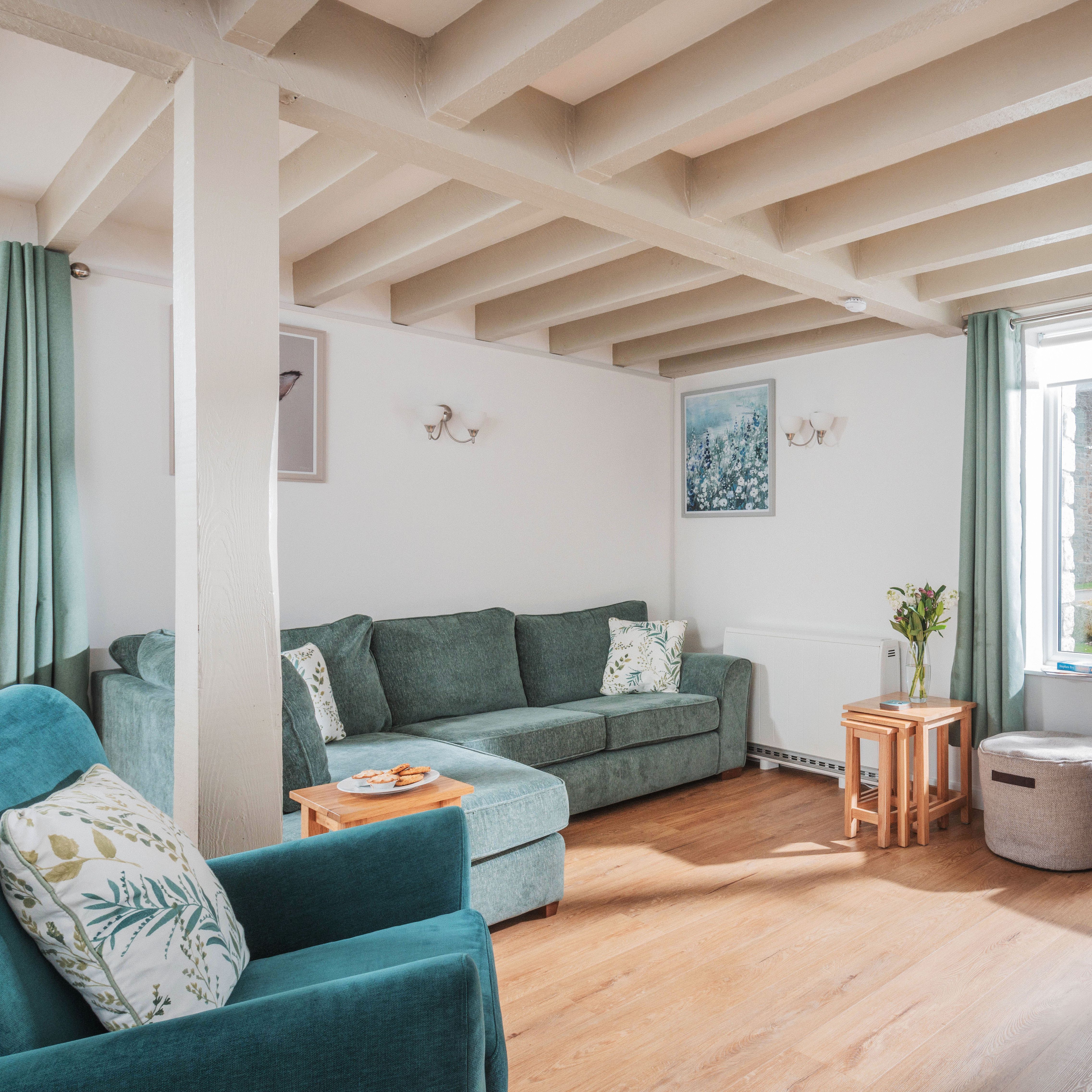 Cozy living room with green sofas, wooden floor, TV, and large window with green curtains